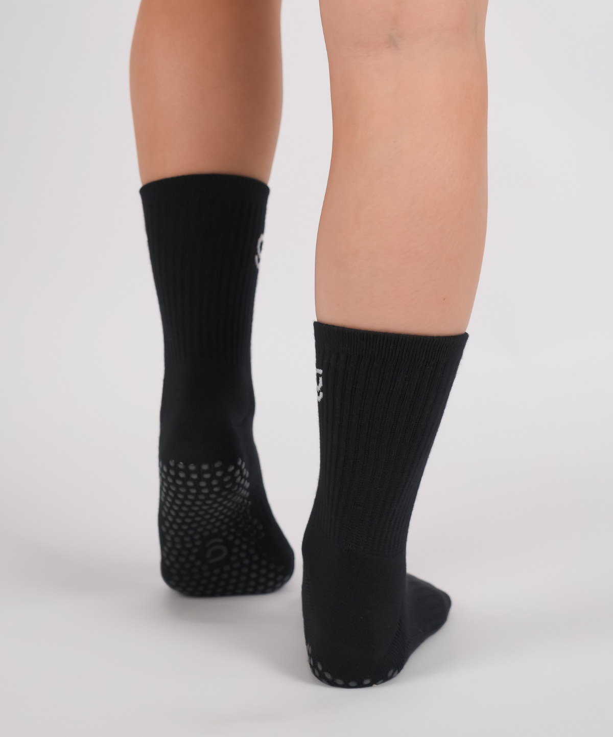 Black socks with grips sole worn by a person on a light gray background