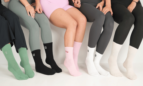 Six models seated side-by-side wearing different colored socks, including green, black, pink, light pink, white, and beige, paired with various leggings.