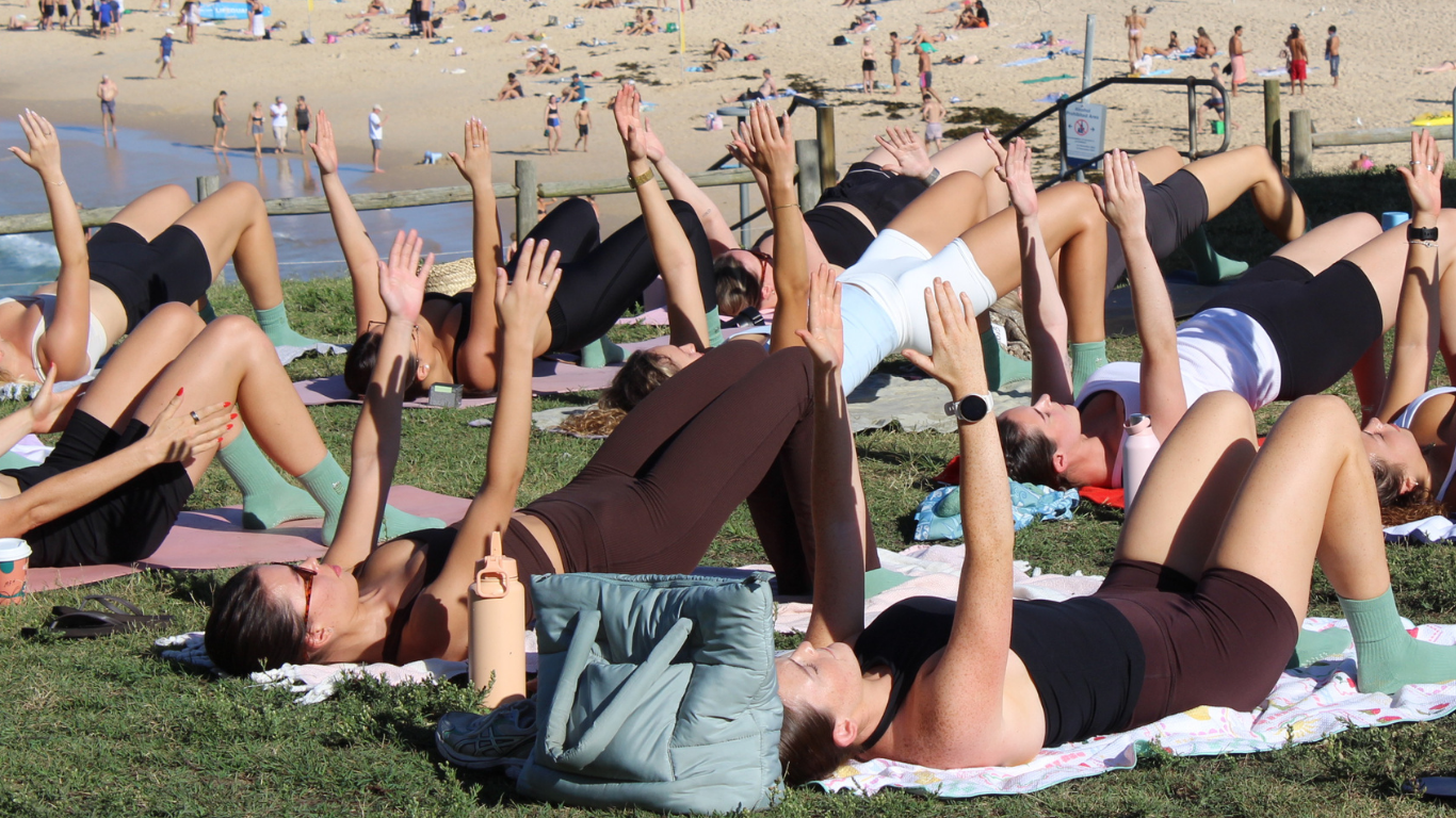 Group of people practicing mat pilates on a grassy area near Bondi Beach
