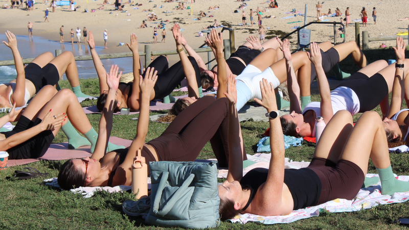 Group of people practicing mat pilates on a grassy area near Bondi Beach