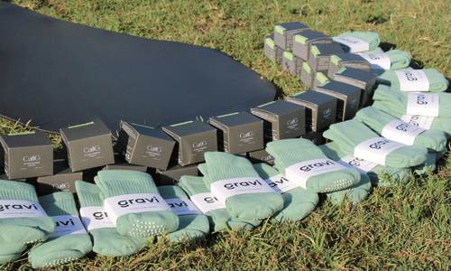 A group of gravi green grip socks with white bands labeled 'gravi' arranged on grass alongside dark gray boxes, with a black mat in the background.