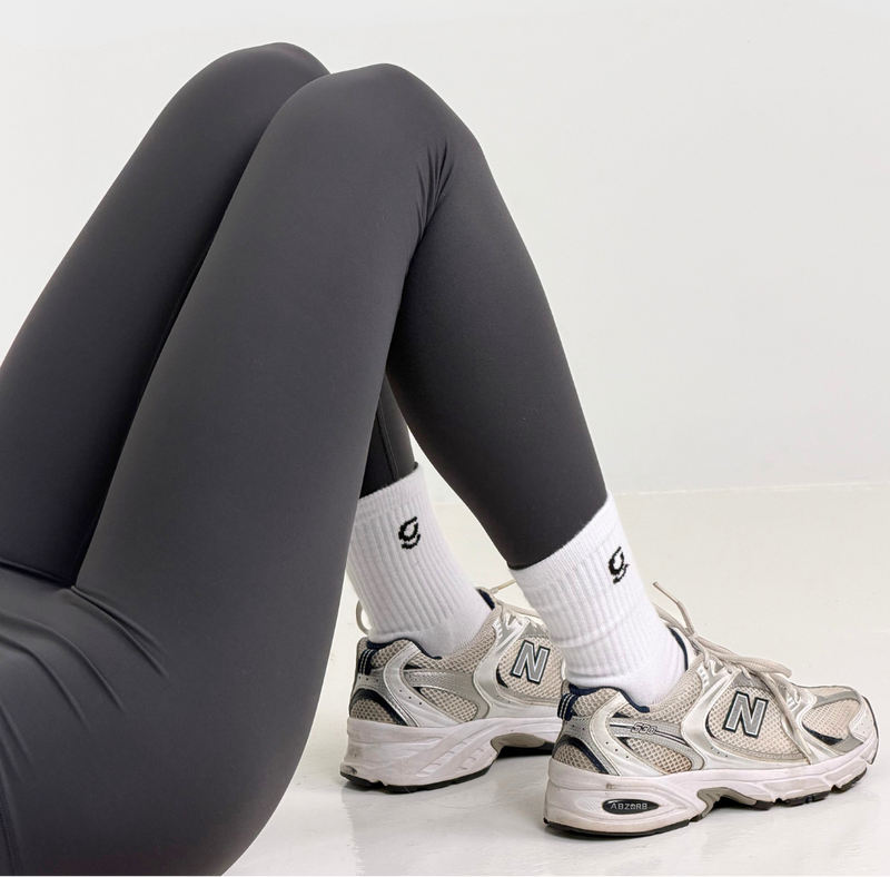 Person wearing dark gray leggings and white sneakers with gravi socks on a light background