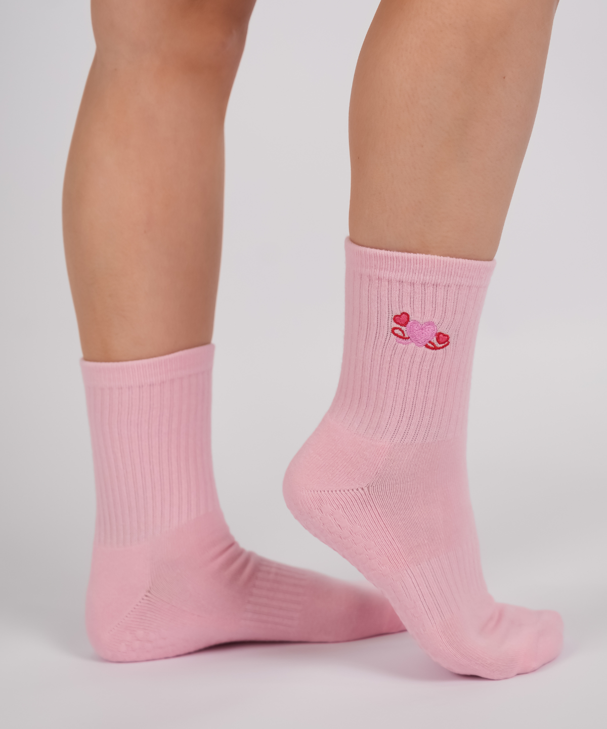 Pink socks with a heart design worn by a person on a light gray background