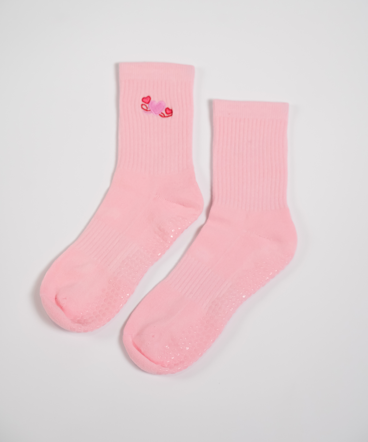 Pair of pink socks with a small red heart design on a light gray background