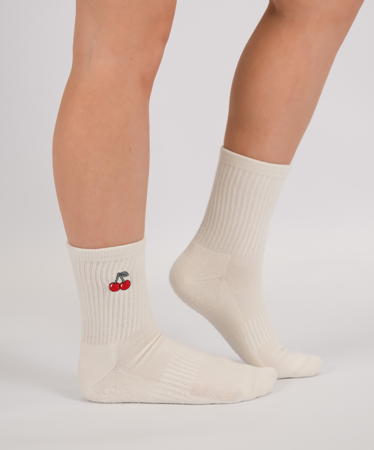 White socks with a cherry design worn by a person on a light gray background