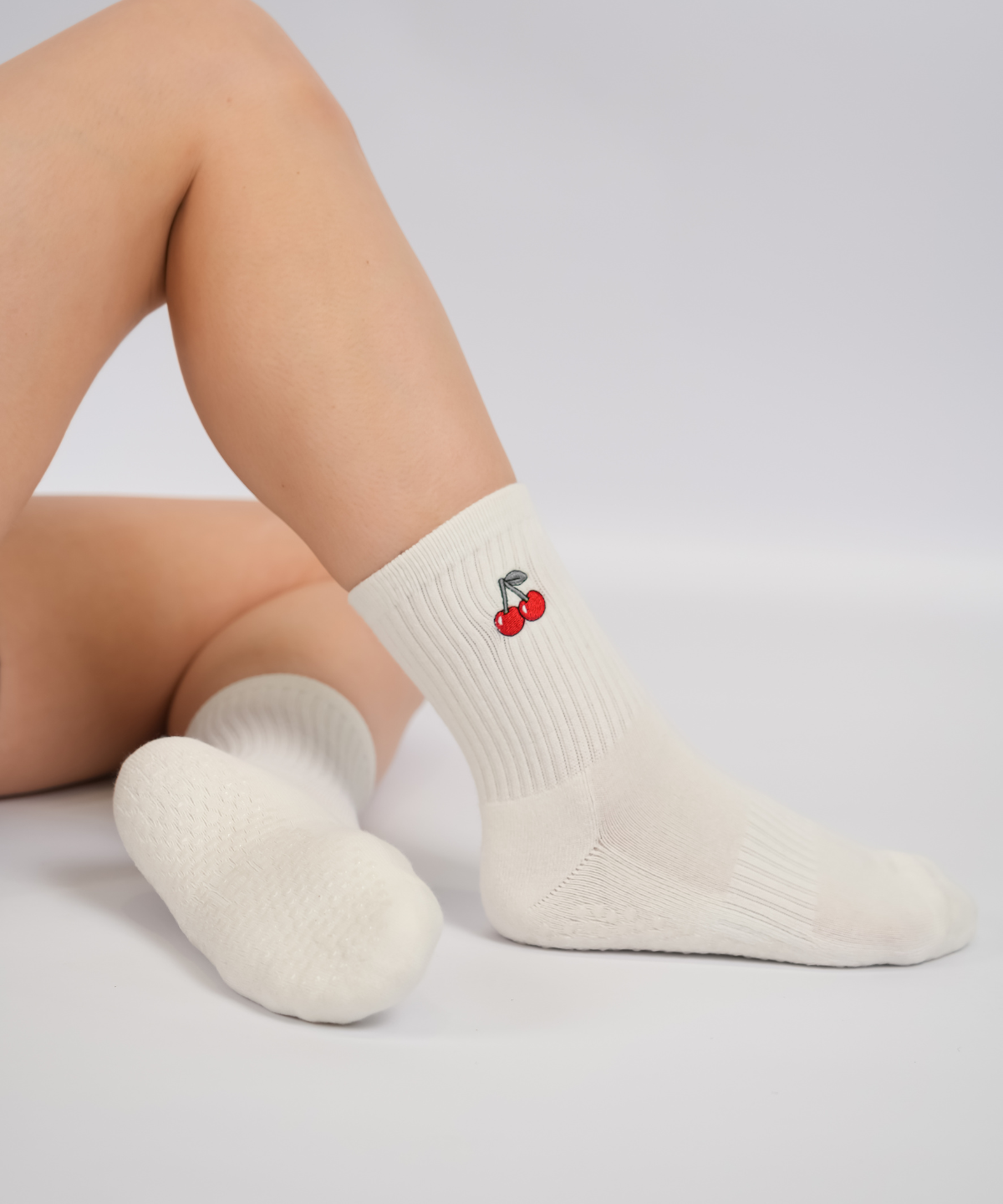 White socks with a cherry design worn by a person on a light gray background